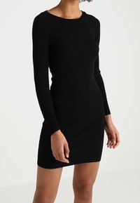 Robe noire à manches longues côtelées, avec un col rond, une silhouette ajustée et une texture lisse, adaptée aux occasions décontractées ou formelles.