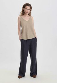 Top senza maniche beige con scollatura a V, abbinato a pantaloni a gamba larga blu navy scuro. Il tessuto appare morbido e leggero, con una vestibilità rilassata.