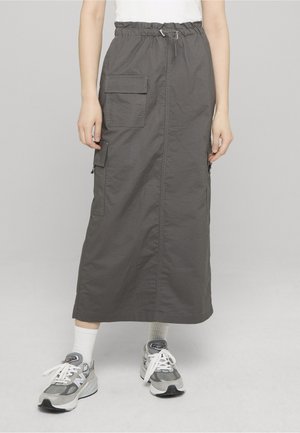 Grauer Midirock mit elastischem Bund und aufgesetzten Taschen vorne, getragen mit weißen Socken und grauen Turnschuhen vor neutralem Hintergrund.