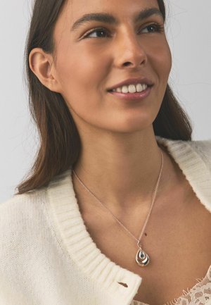 Silver necklace featuring a teardrop pendant with a darker gem accent. Model wears a cream cardigan and lace top, showcasing the jewelry.