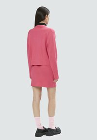 Conjunto de sudadera rosa y falda a juego, de tela suave, corte relajado, textura acanalada, combinado con calcetines rosas y zapatos negros de plataforma.