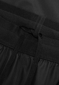 Zwarte sportshorts hebben een gestructureerde elastische tailleband met een trekkoord, vervaardigd uit lichtgewicht stof met een gladde afwerking.