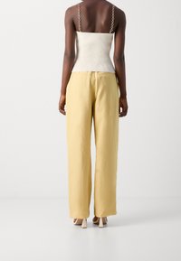 Ribbed cream top with chain straps paired with high-waisted, wide-leg yellow trousers. Smooth texture with a relaxed fit and subtle sheen.