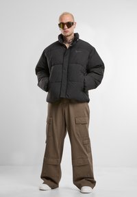 Doudoune noire avec un design matelassé, col haut et boutons sur le devant, associée à un pantalon cargo kaki avec des poches latérales.