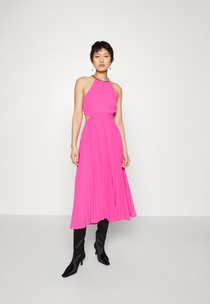 Robe maxi rose à encolure halter avec tissu plissé, côtés découpés et corsage ajusté. Associée à des bottes noires à talons aiguilles arrivant au genou.