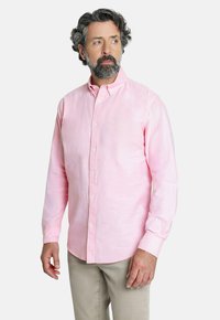 Camisa abotonada rosa claro hecha de una tela texturizada, con cuello y mangas largas, combinada con pantalones beige.