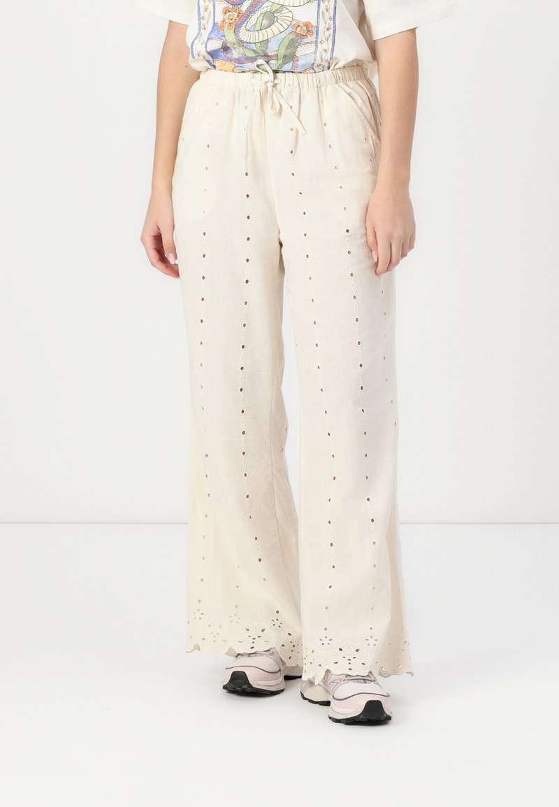 Pantalons légers couleur beige, amples, avec des motifs en œillet et un ourlet festonné. Fabriqués dans un tissu texturé, ils disposent d'une taille élastique et d'un cordon de serrage.