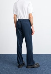 Marinblå träningsbyxor med elastisk midja, vida ben och sidostråk, i kombination med en kortärmad vit skjorta och svarta plattformsskor.