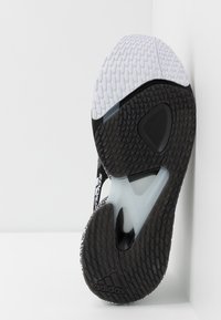 Czarna i biała podeszwa sneakersów o teksturowanej powierzchni, z przezroczystą podeszwą środkową i zaokrąglonym obcasem. Widoczne logo Adidas.