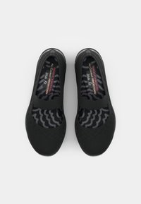 Black slip-on shoes with a textured mesh upper, elastic strap across the top, and a cushioned insole featuring a wave pattern.