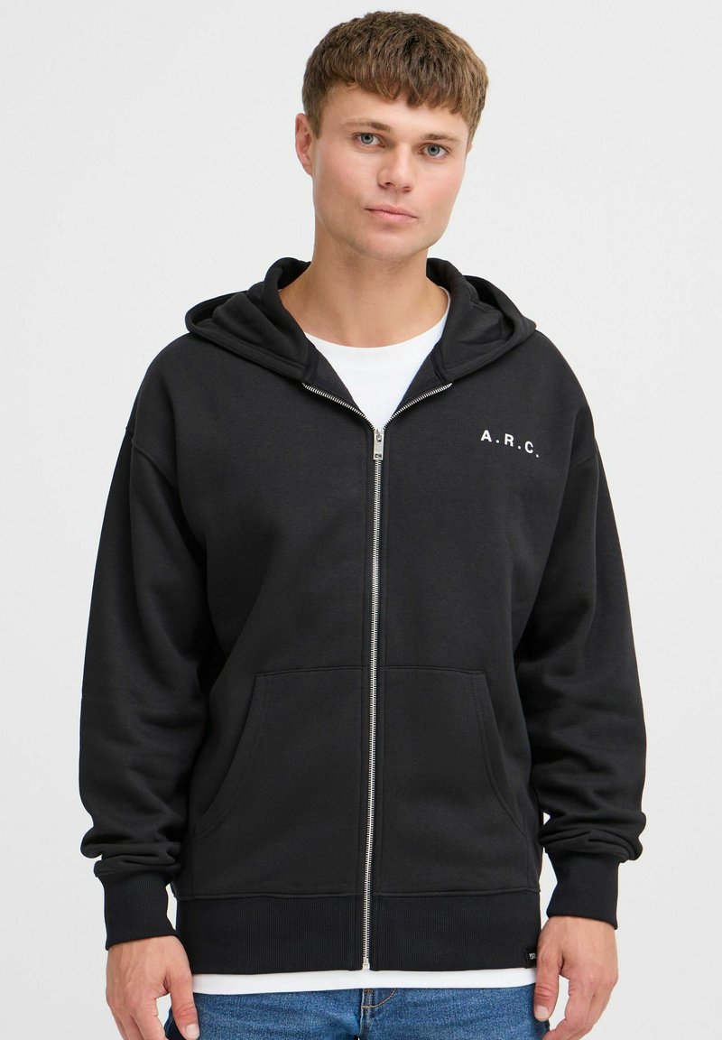 Zwarte hoodie met ritssluiting van sweatstof, met een capuchon, kangoeroezakken en witte "A.R.C." tekst op de borst.