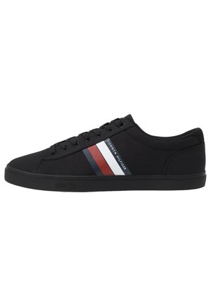 Czarny niskoprofilowy sneaker z sznurowaniem z przodu, płaską podeszwą i czerwono-biało-niebieskimi paskami z logo Tommy Hilfiger po boku.