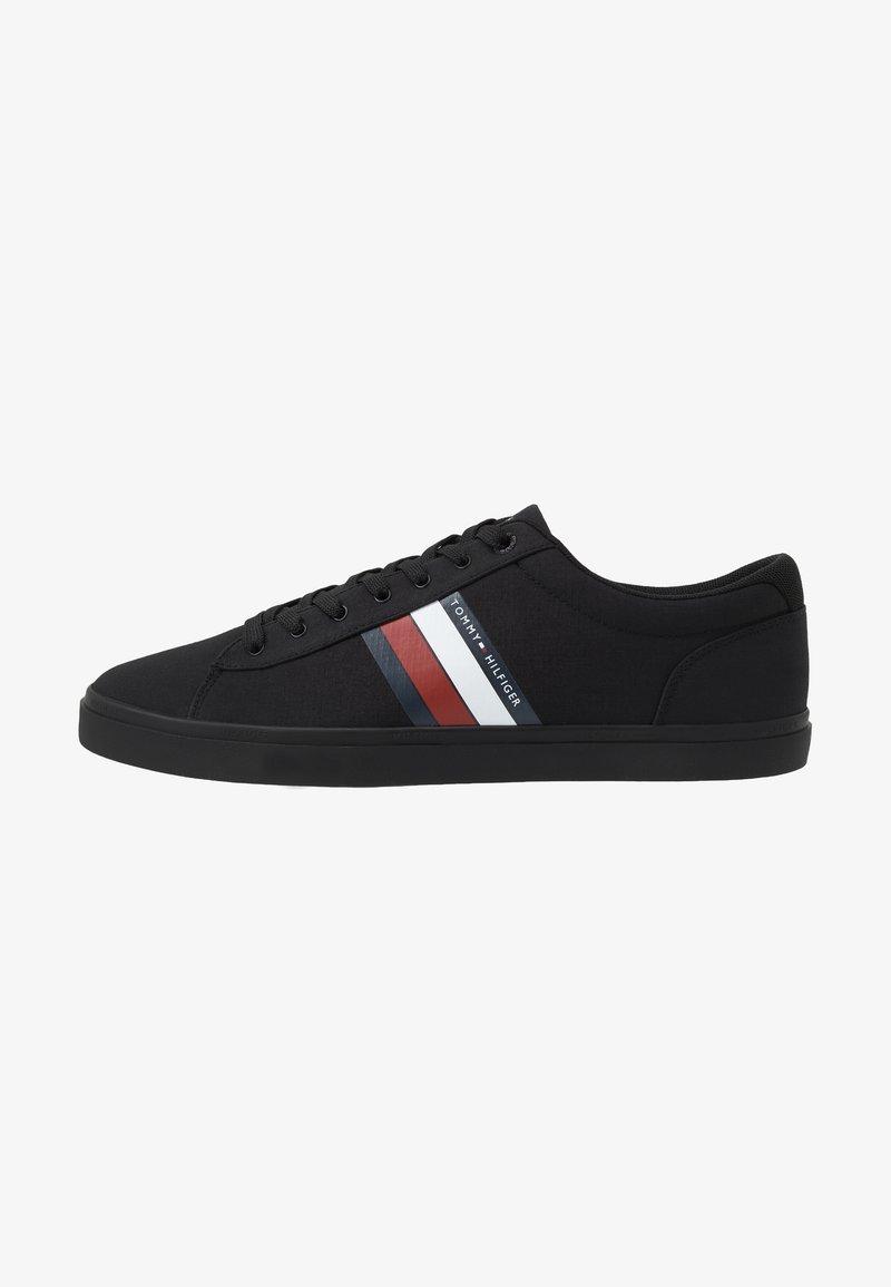 Baskets basses noires à lacets, semelle plate, avec des bandes rouges, blanches et bleues et le logo Tommy Hilfiger sur le côté.