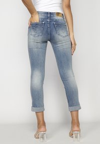 Hellblaue Jeans aus Denim mit taillierter Passform, überschnittenem Saum, geschwungenen Gesäßtaschen und einem hellbraunen Lederetikett am Bund.