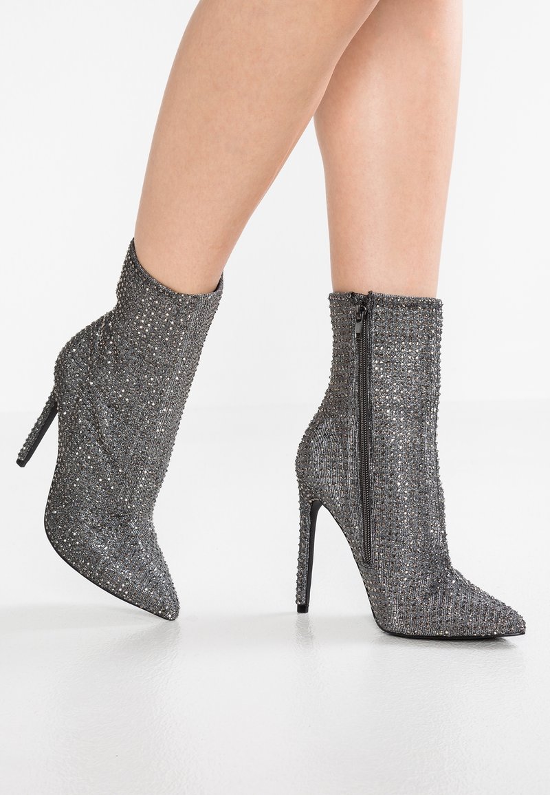 Bottes chevilles grises avec une surface scintillante et texturée, ornées de strass et d'un bout pointu, avec une fermeture éclair latérale et un talon stiletto haut.
