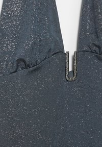 Tummansininen yläosa, jossa kimaltava pinta, kootulla pääntiellä ja keskellä erottuva metallinen U-kirjaimen muotoinen koriste.