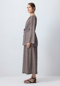 Hnedá vzorovaná dlhá šaty s dlhými rukávmi, s úzkym pásom a sukňou po členky. Nosené s čiernymi sandálmi so sponou.