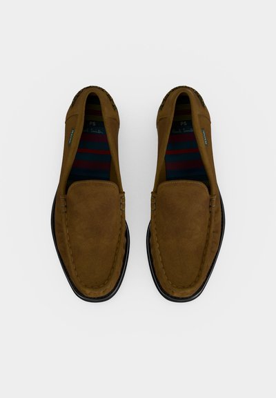Καφέ μοκασίνια από σουέντ με μαύρες σόλες, ορατές ριγέ εσωτερικές σόλες και ραφές, εμφανιζόμενα από πάνω σε λευκό φόντο.