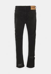 Jeans de mezclilla negra con un detalle desgastado en la parte inferior de la pierna izquierda. Presenta un logotipo en parche en la cintura trasera y bolsillos estándar.