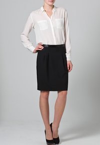 Chemise blanche à boutons avec deux poches poitrine, accompagnée d'une jupe crayon noire et de talons noirs. Tissu lisse, coupe ajustée et design classique.