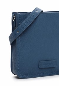 Borsa a tracolla in pelle blu con superficie testurizzata, dotata di una tracolla con marchio e design a corpo rettangolare, dettagli in metallo argento.