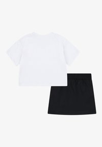 Dvoudílný outfit: bílý bavlněný tričko s krátkým rukávem a kulatým výstřihem a černá sukně s elastickým pasem a hladkou texturou.