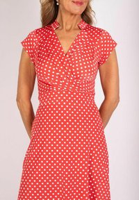 Rotes Kleid mit weißen Punkten, kurzen Kapellärmen, plissiertem Oberteil und taillierter Taille, mit einem V-Ausschnitt und einem ausgestellt Rock.