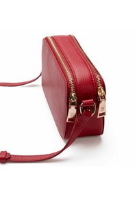 Rote Ledertasche mit strukturiertem Oberflächen, doppelten Reißverschlüssen in Goldfarbe und einem abnehmbaren Trageriemen. Rechteckige Form, flaches Design, ohne sichtbare Logos.