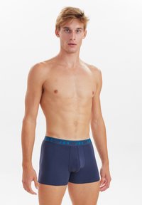 Boxers de color marino con una cinturilla en tono teal que presenta el logo 'JBS'; fabricados con un tejido suave y elástico con un diseño ajustado.