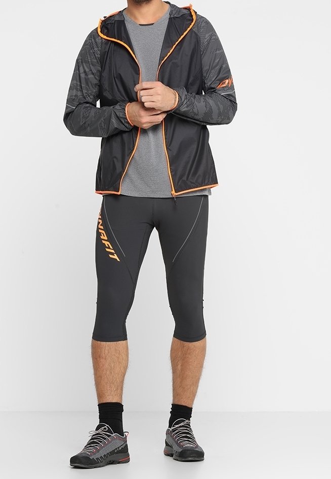 Svart och grå idrottsjacka med orange detaljer, parat med grå kompressionsleggings som har en logotyp och kontrasterande sömmar.