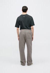 Rückansicht eines Mannes, der ein schwarzes kurzärmeliges T-Shirt und graue Jogginghosen mit Tasche trägt. Der Stoff wirkt weich und lässig im Design.