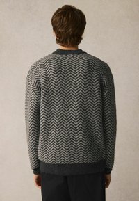 Strickpullover in dunkelgrau und hellgrau im Fischgrätenmuster, mit einem gerippten Kragen und Bündchen, und einem weichen, strukturierten Finish.