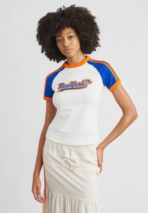 Λευκό κοντομάνικο μπλουζάκι με μπλε και πορτοκαλί λεπτομέρειες, με γραφικό "New York". Συνδυασμένο με φούστα κρεμ χρώματος με βολάν.