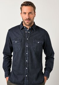Camicia in denim scuro con bottoni, dotata di due tasche sul petto, maniche lunghe e colletto classico. Il tessuto ha una finitura liscia con cuciture visibili.
