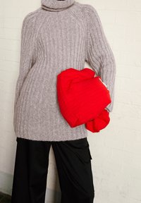 Ljust grå ribbade polotröja med långa ärmar, i kombination med svarta vida byxor. Röd quiltad accessoar draperad över armen.