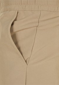 Gros plan d'une poche de pantalon en tissu beige avec des coutures détaillées et de légers plis.