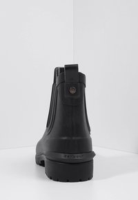 Bottes de cheville noires imperméables en caoutchouc, avec des panneaux latéraux élastiques, une languette de tirage et une semelle texturée avec "Barbour" en relief.