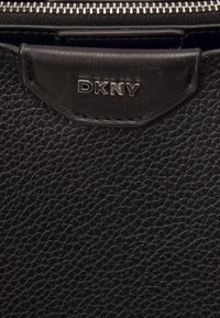 Czarna skórzana torebka o teksturowanej powierzchni, wyposażona w srebrny zamek błyskawiczny oraz zawieszkę z logo "DKNY" w metalicznych literach.
