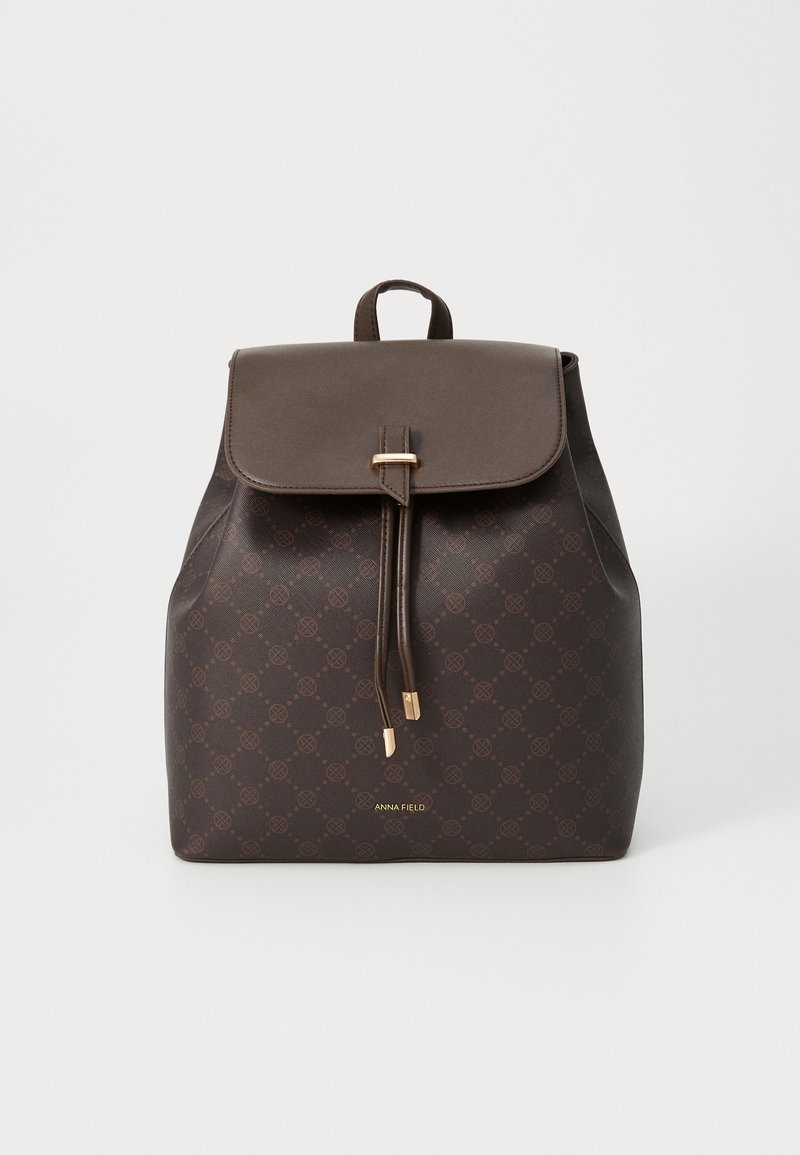 Sac à dos marron à motif avec un rabat, cordon de serrage et accents en métal doré. Texture lisse avec détail du logo à la base.