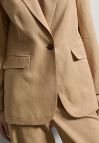 Beige Leinensakko mit einem Knopfverschluss, Reverskragen und zwei seitlichen Taschen. Strukturiertem Stoff mit weichem Finish.