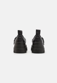 Black platform sneakers with a smooth, shiny finish, featuring textured accents and pull tabs at the heel for easy wear.