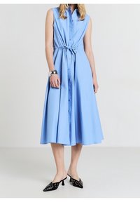 Jasnoniebieska, bezrękawnikowa sukienka z zapięciem na guziki z przodu i ściągaczem w talii. Długość do połowy łydki, zwiewna spódnica, zestawiona z czarnymi szpilkami w szpic.