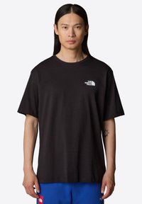 Camiseta negra de manga corta hecha de algodón con cuello redondo, que presenta un pequeño logotipo blanco en el lado izquierdo del pecho. Textura suave.