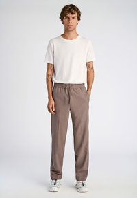 Bruna, lätta, skräddarsydda byxor med resårmidja och sidofickor, tillsammans med en enkel vit T-shirt med rund halsringning och sneakers.