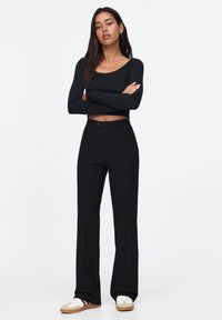 Zwarte aansluitende longsleeve top en hoogwaist zwarte broek met een rechte pijpdesign, met een sluiting met een knoop aan de voorkant en een gladde textuur.
