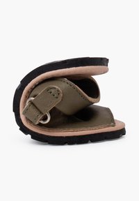 Sandalia de cuero verde oliva con un diseño flexible y plegable, que presenta un acento de cuero marrón y una suela de goma negra texturizada.