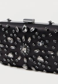 Čierna saténová kabelka ozdobená rôznymi priesvitnými a kryštáľovými dekoráciami v rôznych tvaroch. Obsahuje strieborný uzáver.