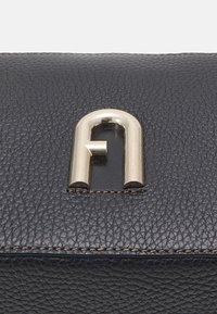 Černá texturovaná kožená kabelka se stříbrným kovovým zapínáním ve tvaru obloukového zámku ve středu.