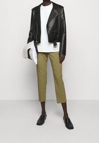 Zwarte leren motorjacket, witte t-shirt, olijfgroene cropped broek en zwarte instapschoenen. Opmerkelijke details zijn de ritsen van de jacket en de riemgesp.