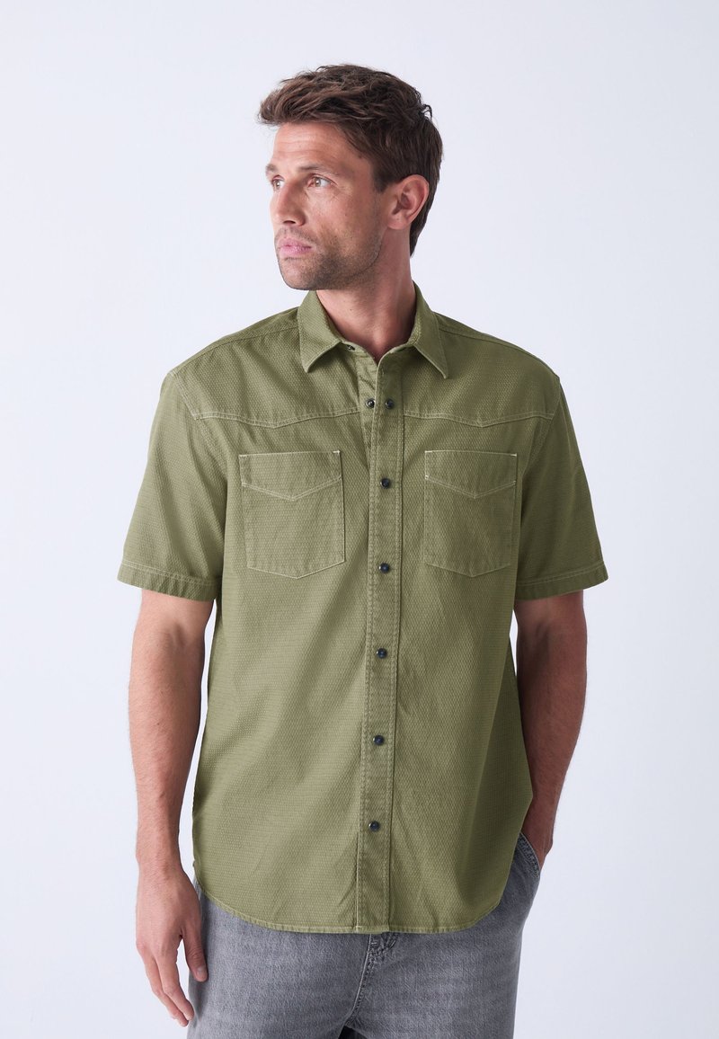 Short-sleeve, olive green shirt made of textured fabric, featuring two chest pockets, black buttons, and a standard collar.